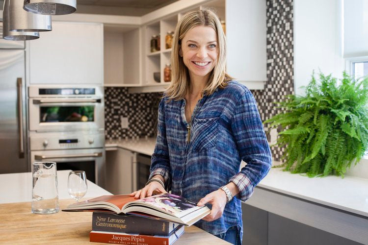 Trish wearing blue plaid shirt standing at kitchen island with cookbooks